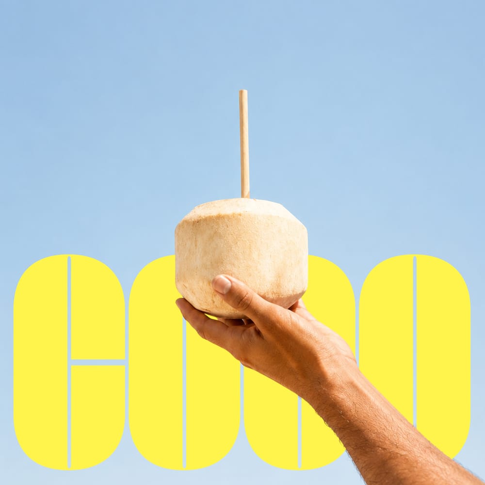 Hand holding coconut drink with bold yellow COCO typography on sky blue background