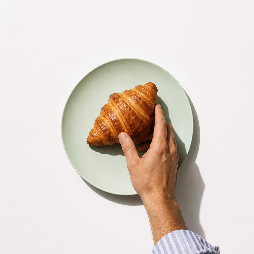 Hand holding croissant on white plate minimal food photography overhead