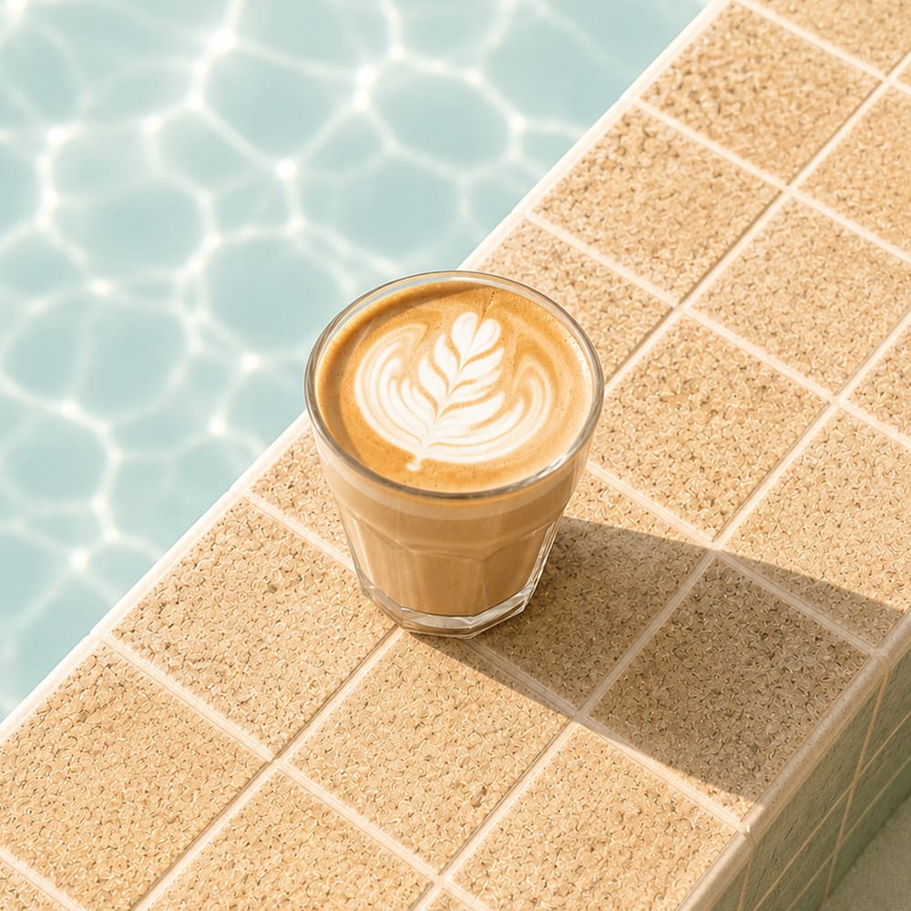 Latte art coffee cup beside turquoise pool tiles in warm morning light