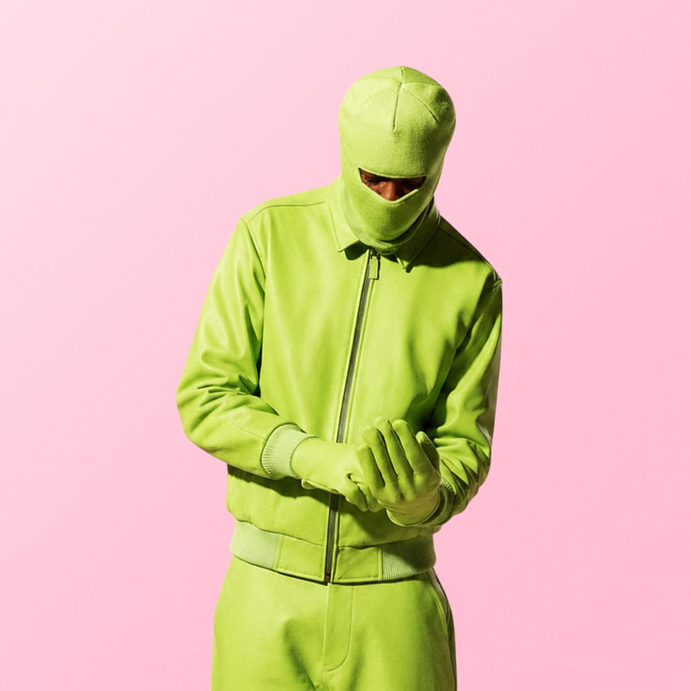 Person in bold green suit standing against soft pink background fashion editorial photography