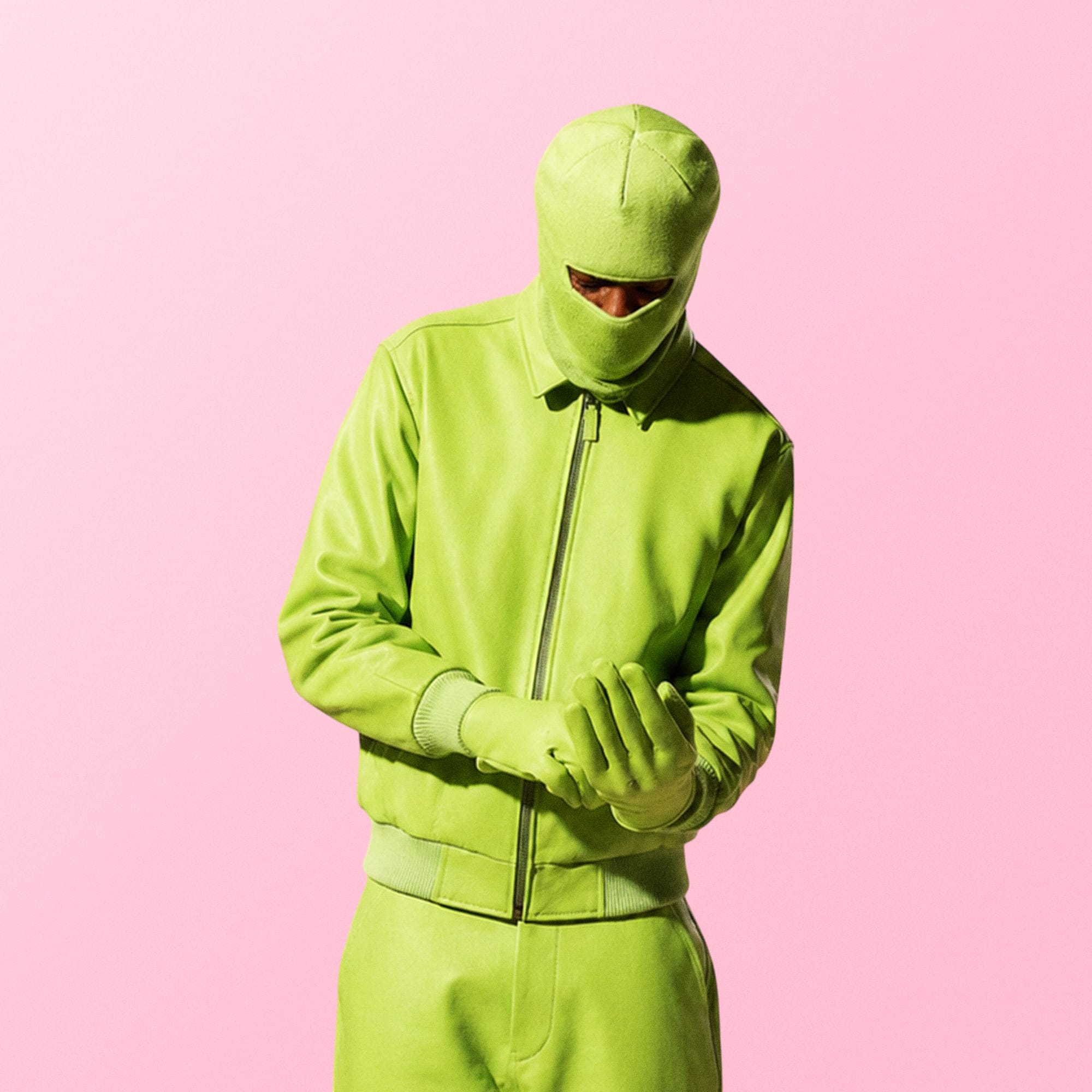 Person in bold green suit standing against soft pink background fashion editorial photography