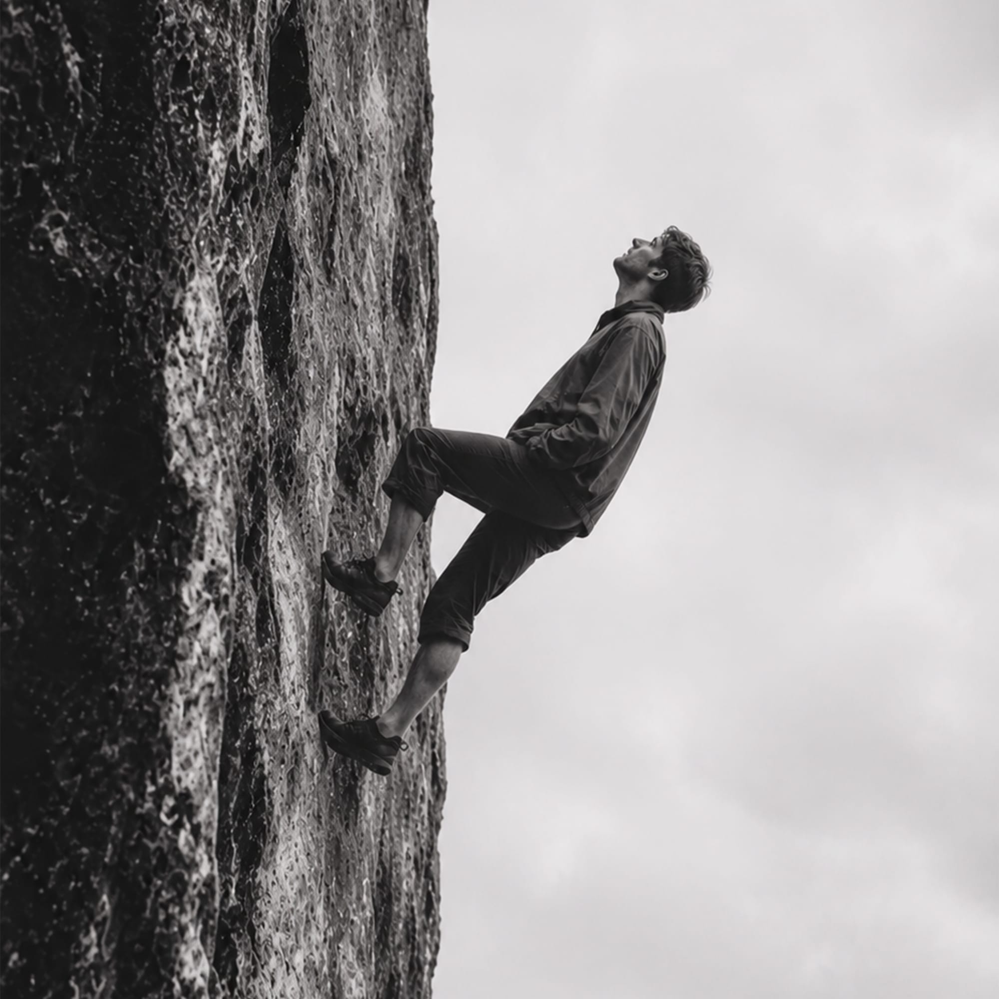 Person rock climbing on textured stone wall black and white photography